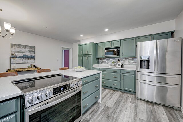 kitchen featuring decorative backsplash, light hardwood / wood-style floors, green cabinetry, stainless steel appliances, and decorative light fixtures