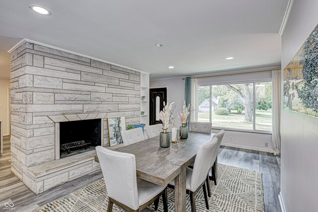 dining room with crown molding, a stone fireplace, and hardwood / wood-style floors