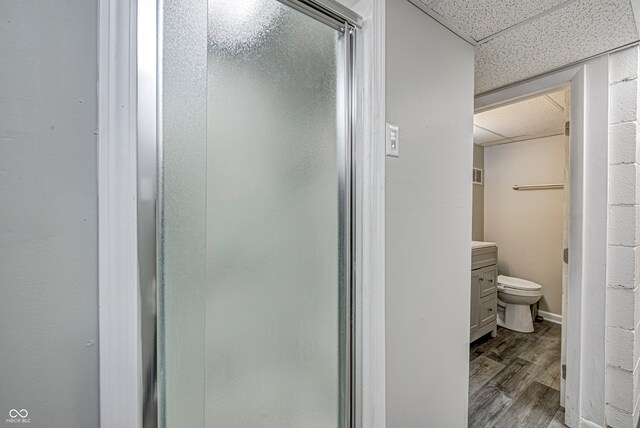 bathroom with hardwood / wood-style flooring, a drop ceiling, walk in shower, vanity, and toilet