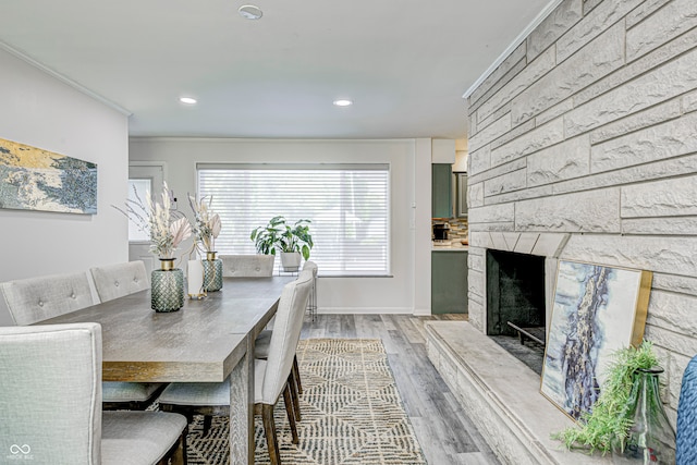 dining space featuring light wood-type flooring, ornamental molding, and a high end fireplace