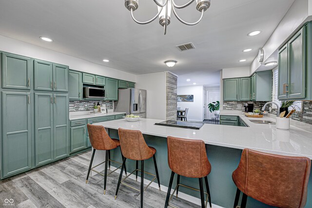 kitchen with appliances with stainless steel finishes, a breakfast bar, kitchen peninsula, light wood-type flooring, and sink