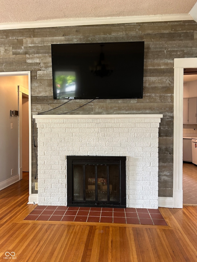 interior details with white dishwasher, ornamental molding, a textured ceiling, a tiled fireplace, and hardwood / wood-style flooring