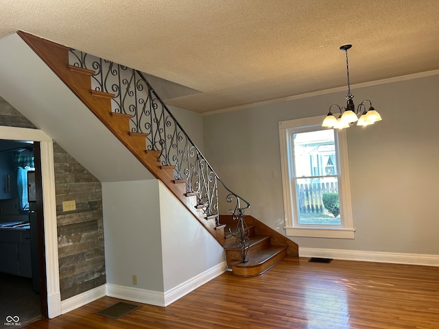 staircase with crown molding, hardwood / wood-style floors, a notable chandelier, lofted ceiling, and a textured ceiling