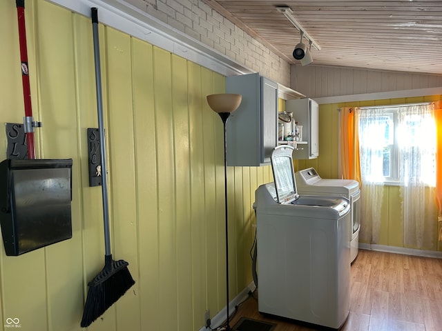 laundry area featuring brick wall, light hardwood / wood-style floors, wood walls, and washer and clothes dryer