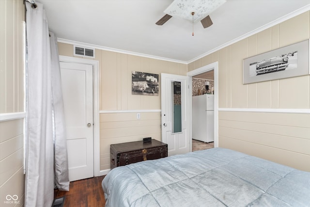 bedroom with ornamental molding, white fridge, wood walls, dark wood-type flooring, and ceiling fan