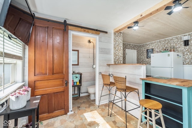 kitchen with white fridge, butcher block counters, a barn door, wood walls, and ceiling fan