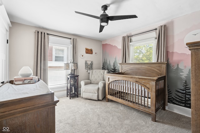 bedroom with multiple windows, ceiling fan, light colored carpet, and a nursery area