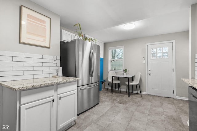 kitchen featuring stainless steel fridge, white cabinets, and light stone countertops