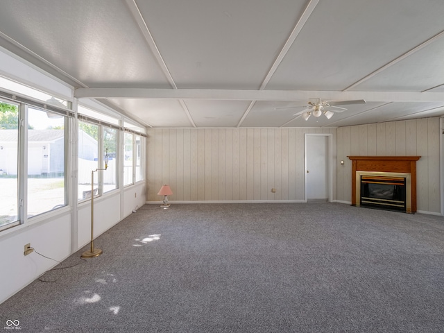 unfurnished living room featuring carpet floors, wood walls, and ceiling fan