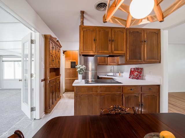 kitchen featuring stainless steel fridge, sink, kitchen peninsula, black electric cooktop, and vaulted ceiling