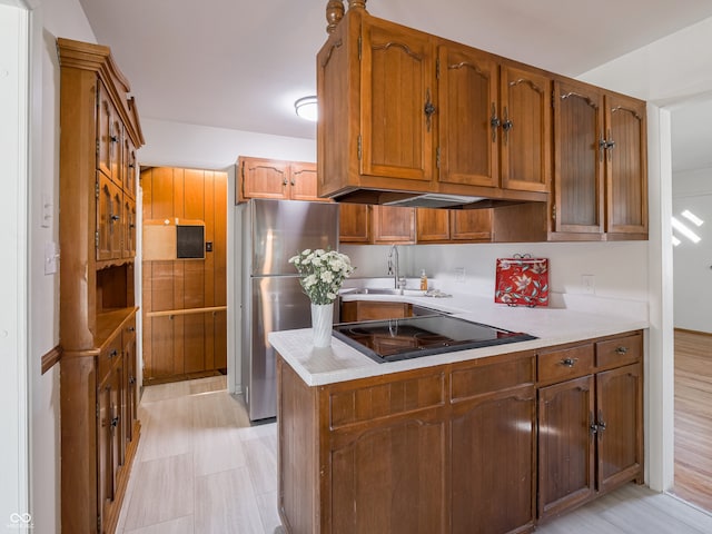 kitchen featuring stainless steel fridge, kitchen peninsula, black cooktop, light wood-type flooring, and sink