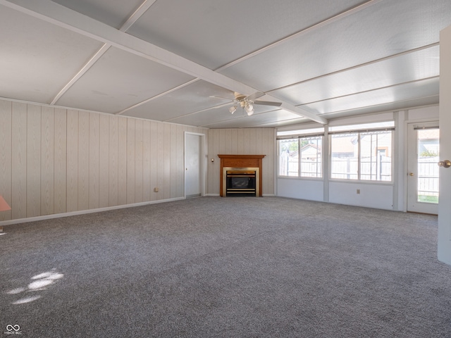 unfurnished living room with carpet floors, wood walls, ceiling fan, and a wealth of natural light