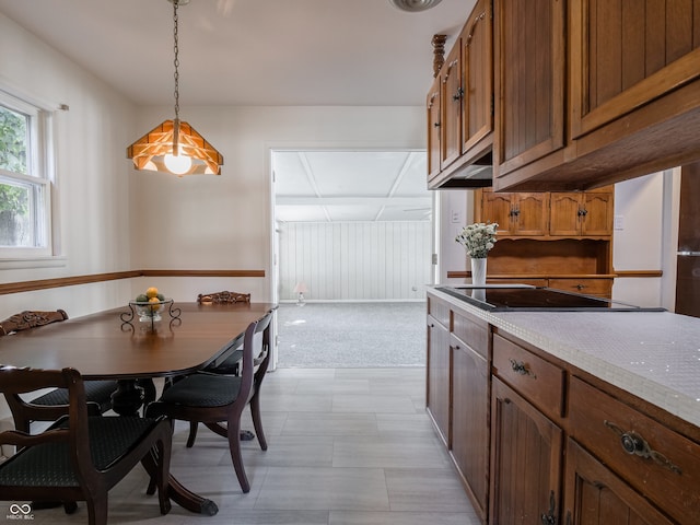 kitchen featuring light stone counters, light colored carpet, decorative light fixtures, and black electric stovetop