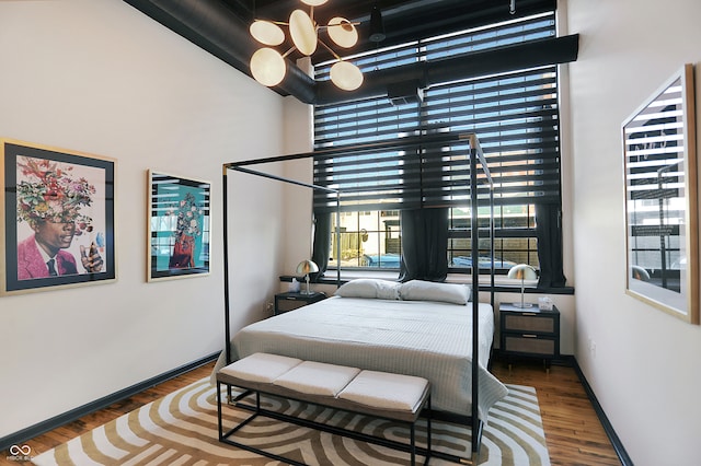 bedroom with an inviting chandelier, dark hardwood / wood-style floors, and a high ceiling