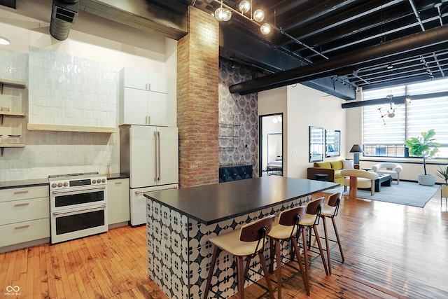 kitchen featuring light wood-type flooring, backsplash, white cabinetry, a high ceiling, and high quality appliances