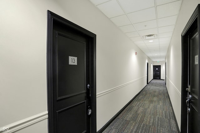 hallway with dark carpet and a paneled ceiling