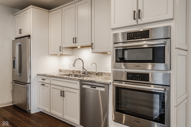 kitchen with white cabinets, light stone countertops, dark hardwood / wood-style flooring, stainless steel appliances, and sink