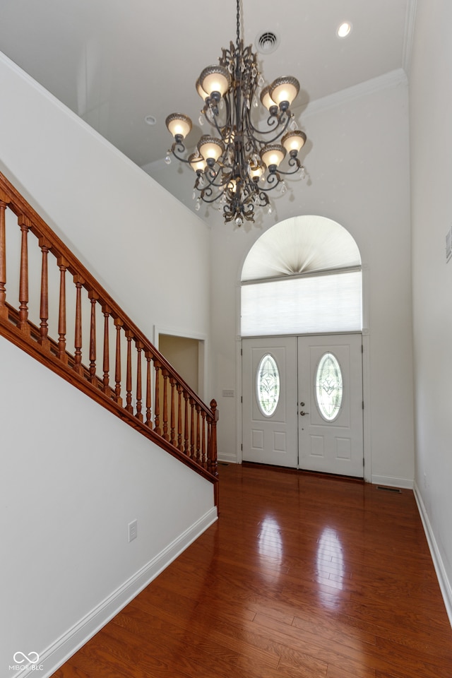 foyer entrance featuring ornamental molding, a high ceiling, a notable chandelier, and hardwood / wood-style flooring