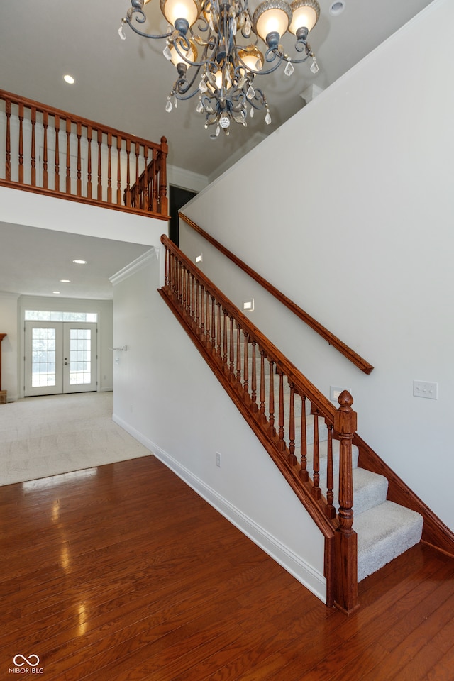 staircase featuring ornamental molding, a notable chandelier, french doors, and wood-type flooring