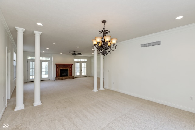 unfurnished living room featuring ornate columns, crown molding, a brick fireplace, light colored carpet, and ceiling fan with notable chandelier