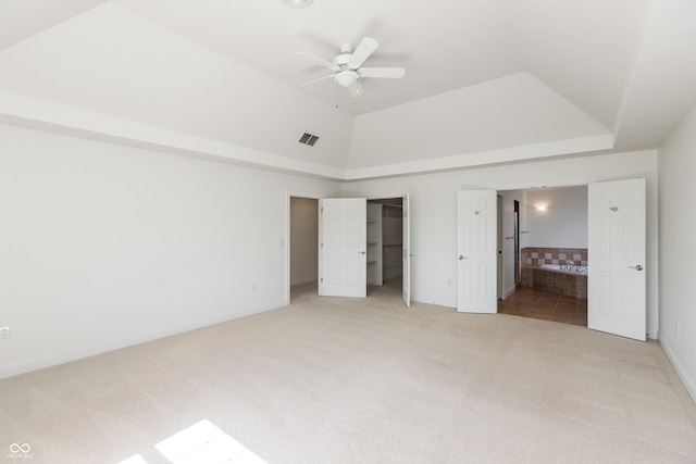 unfurnished bedroom featuring light colored carpet, ceiling fan, a walk in closet, and ensuite bath