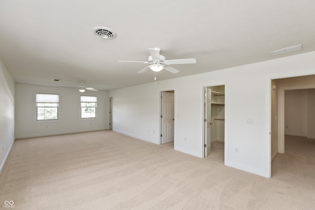 unfurnished bedroom featuring a closet, ceiling fan, light carpet, and a walk in closet