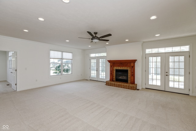 unfurnished living room featuring french doors, crown molding, a brick fireplace, and light colored carpet