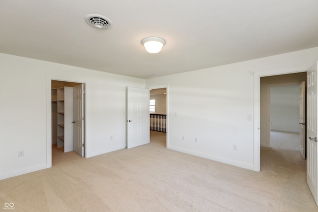 unfurnished bedroom featuring a spacious closet, a closet, and light colored carpet