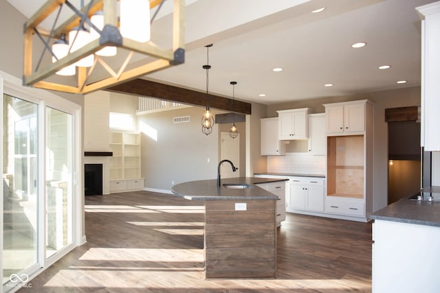 kitchen with an island with sink, tasteful backsplash, white cabinets, dark hardwood / wood-style flooring, and sink