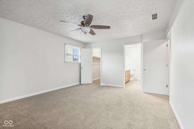 unfurnished bedroom featuring ceiling fan, a textured ceiling, a closet, and a walk in closet