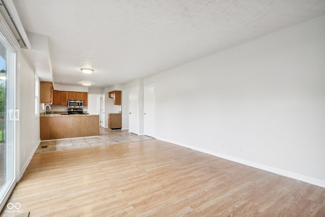 unfurnished living room with light wood-type flooring, a textured ceiling, and sink