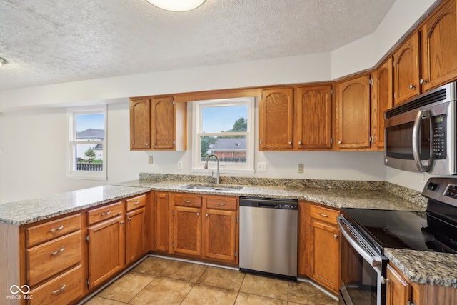 kitchen with light stone counters, sink, kitchen peninsula, a textured ceiling, and stainless steel appliances