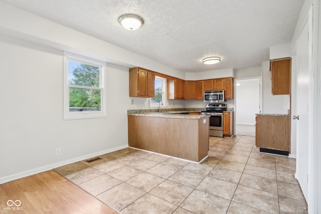 kitchen with a textured ceiling, kitchen peninsula, light wood-type flooring, and stainless steel appliances