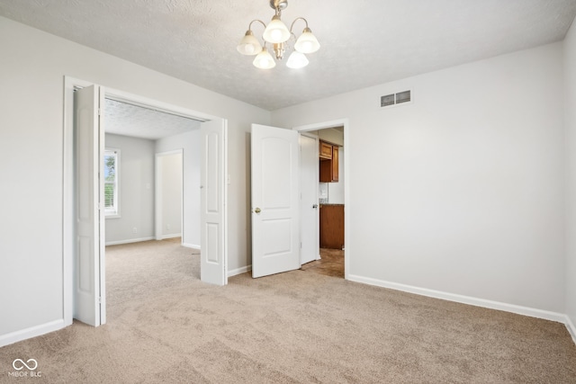 unfurnished bedroom with a chandelier, a textured ceiling, and light colored carpet