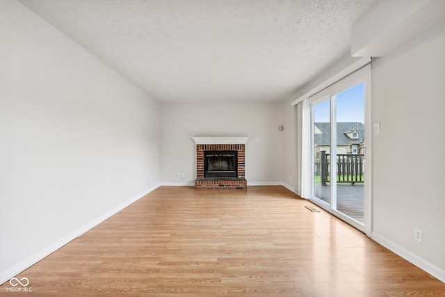 unfurnished living room with a textured ceiling, light hardwood / wood-style floors, and a brick fireplace