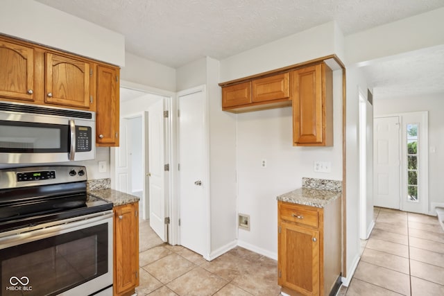 kitchen with light stone countertops, stainless steel appliances, a textured ceiling, and light tile patterned flooring