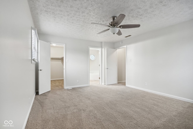 unfurnished bedroom with a spacious closet, a closet, a textured ceiling, carpet flooring, and ceiling fan