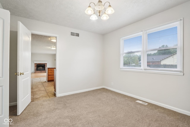 unfurnished room featuring a notable chandelier, a brick fireplace, a textured ceiling, and light colored carpet