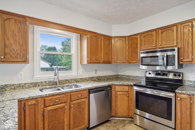 kitchen with light stone counters, light tile patterned floors, stainless steel appliances, a textured ceiling, and sink