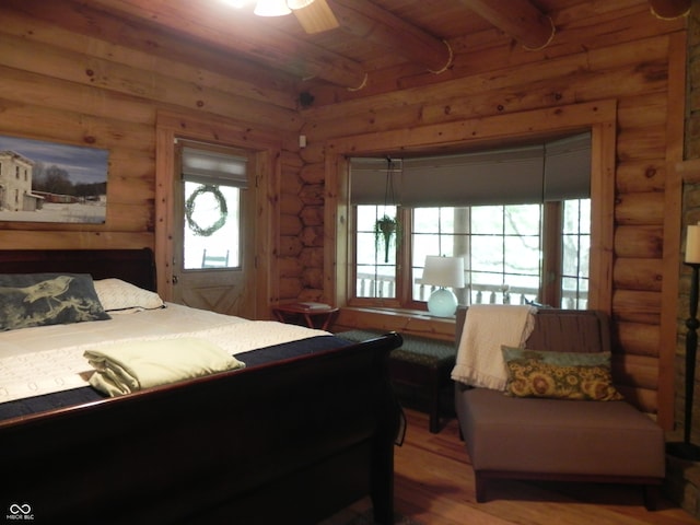 bedroom with hardwood / wood-style floors, ceiling fan, wooden ceiling, beam ceiling, and rustic walls