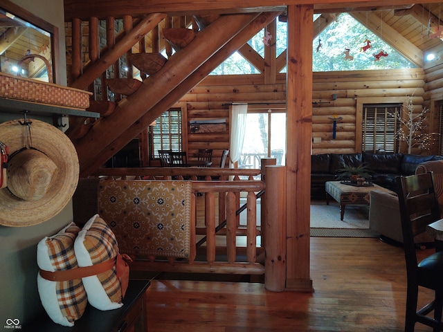 staircase with beam ceiling, high vaulted ceiling, wood-type flooring, and rustic walls