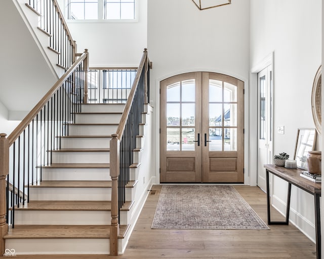 entrance foyer featuring light wood-type flooring, a towering ceiling, and french doors