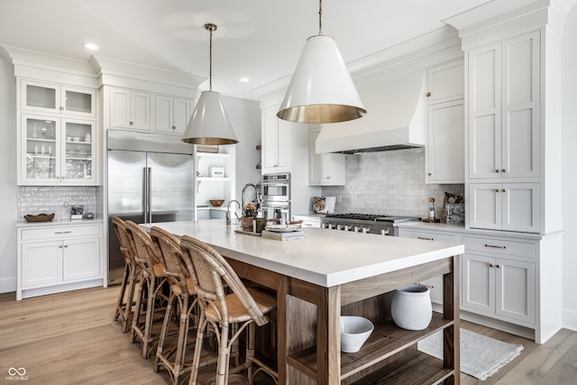 kitchen featuring decorative light fixtures, stainless steel appliances, a breakfast bar, light wood-type flooring, and decorative backsplash