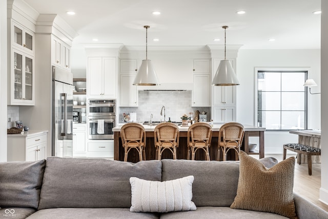 kitchen with decorative backsplash, light hardwood / wood-style floors, white cabinets, pendant lighting, and stainless steel appliances