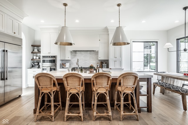 kitchen featuring white cabinets, a kitchen island with sink, appliances with stainless steel finishes, and hanging light fixtures