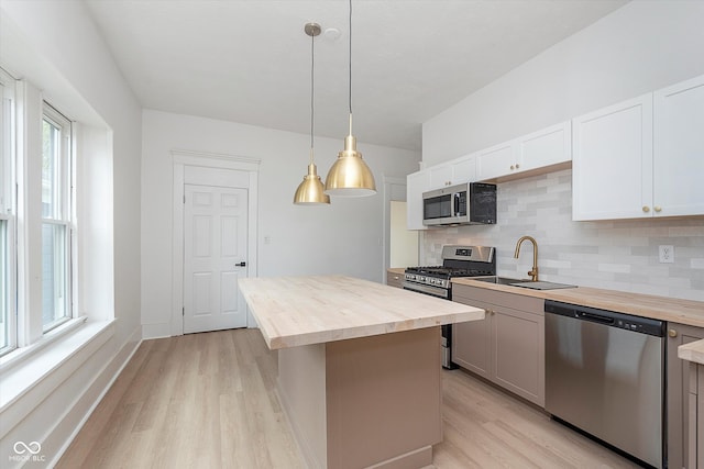 kitchen featuring white cabinetry, butcher block counters, stainless steel appliances, and decorative light fixtures