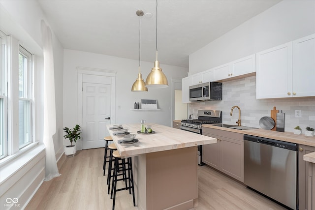 kitchen with white cabinets, pendant lighting, a kitchen island, stainless steel appliances, and light wood-type flooring