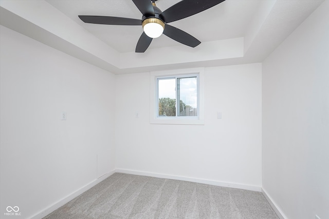 carpeted spare room with a tray ceiling and ceiling fan