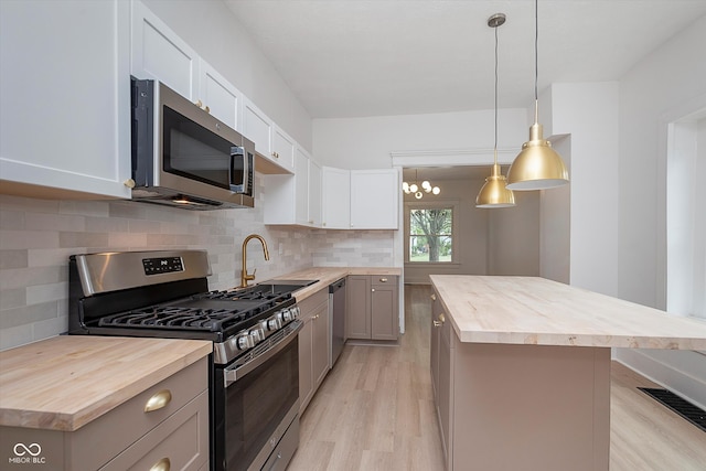 kitchen featuring butcher block countertops, pendant lighting, stainless steel appliances, a center island, and sink