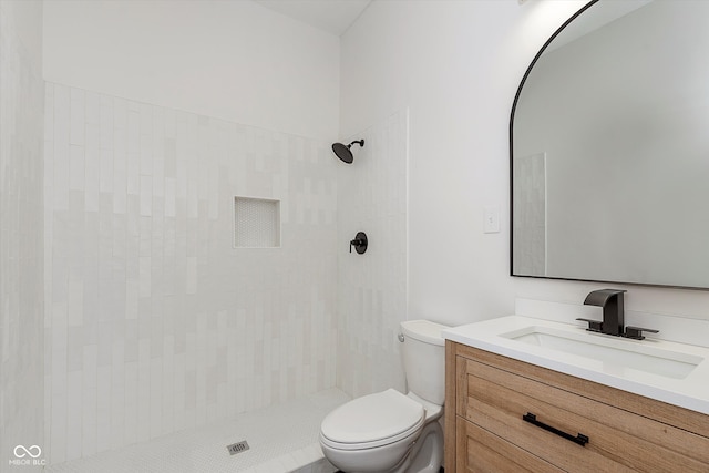 bathroom featuring a tile shower, vanity, and toilet